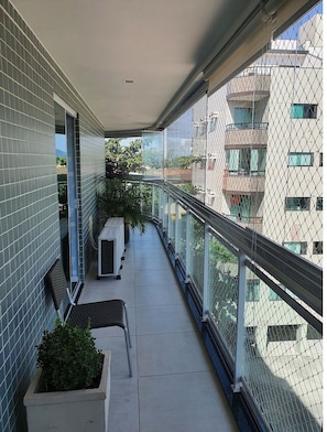 A balcony with a metal railing, a row of chairs, and potted plants.