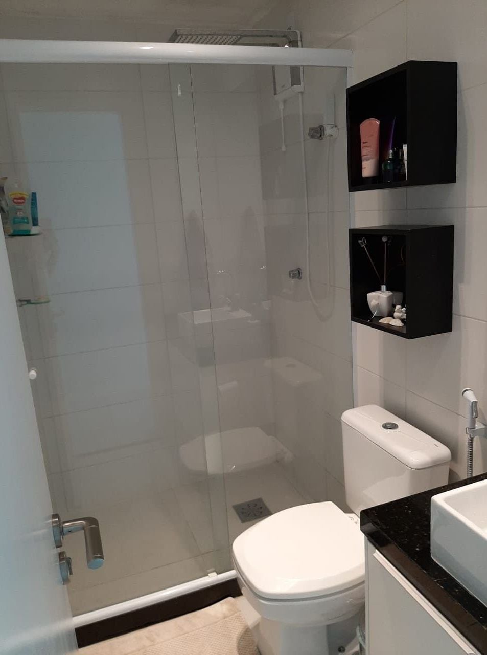A bathroom with a glass-enclosed shower, a white toilet, and black shelves with toiletries.
