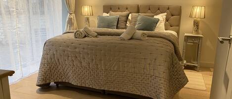 A neatly made bed with a quilted cover, two bedside lamps, and a small bedside table with a vase.