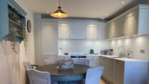 A modern kitchen with white cabinets, a round dining table, and a hanging pendant light. - Walcot Yard in Bath (Bath)