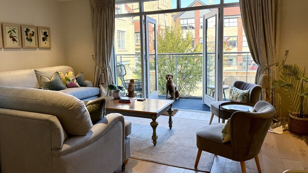 A modern living room with a sofa, armchair, and coffee table. A dog sits by the window, which offers a view of the city. - Walcot Yard in Bath (Bath)