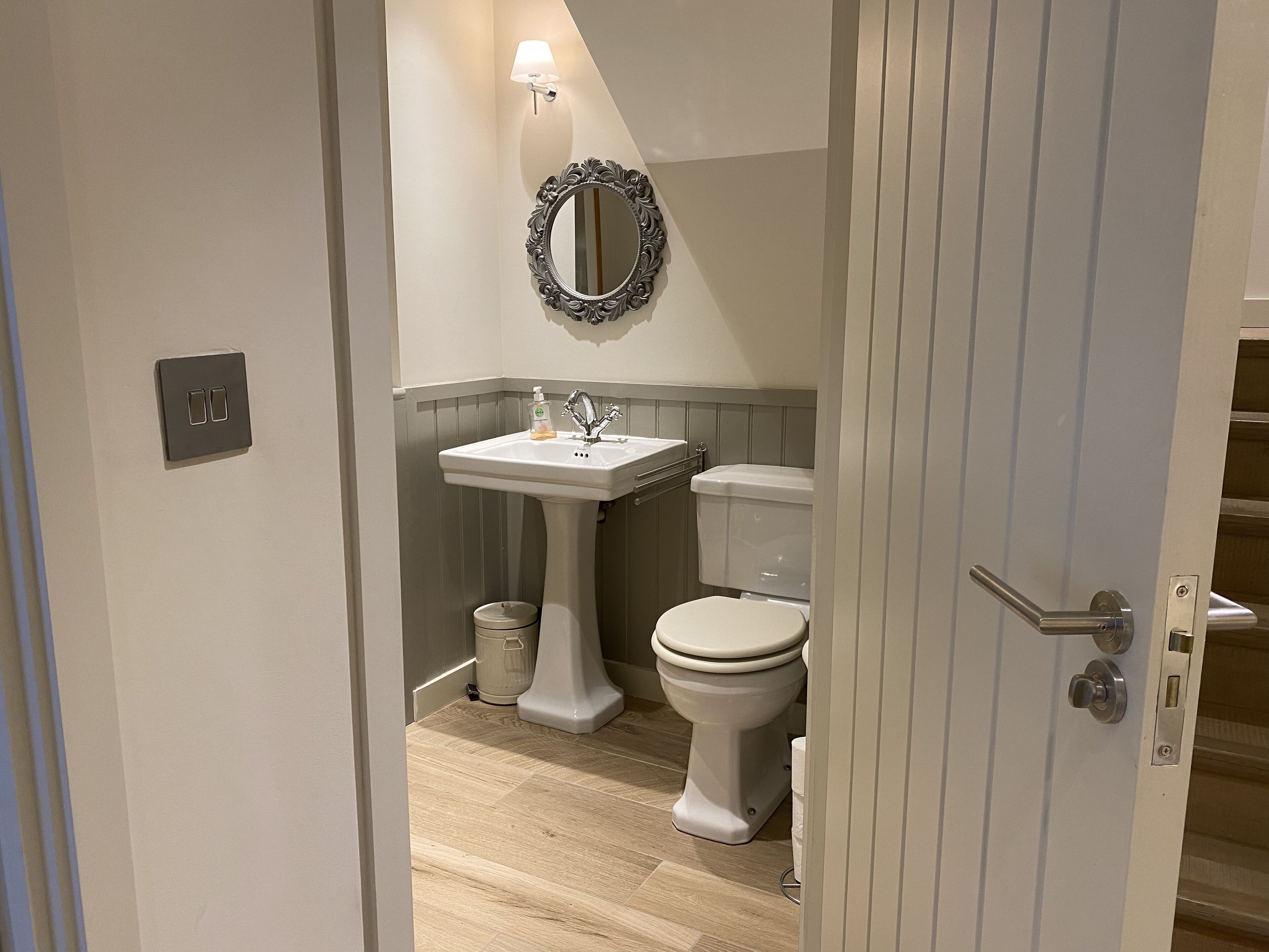 Une salle de bain avec un lavabo sur colonne, des toilettes et un miroir fixé au mur.