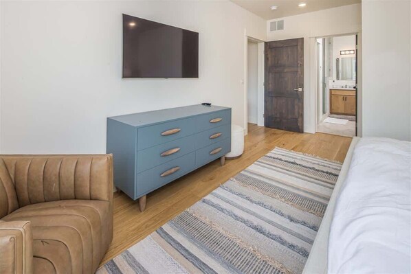Un dormitorio con cama, un aparador azul, televisor y puerta de madera.