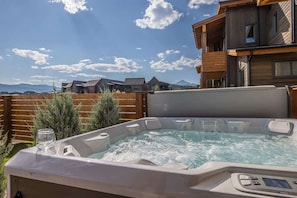 A hot tub in a backyard with a wooden fence and a mountain in the background. - Opulent 4 Bedroom Townhouse (Big Sky)