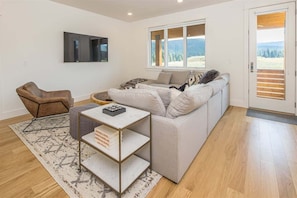 Un salon moderne avec un canapé, une table basse et un fauteuil. Une fenêtre offre une vue sur l’extérieur.