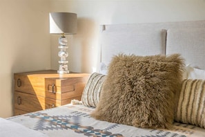 Une chambre Ă coucher avec un lit, une commode en bois, une lampe et un oreiller moelleux.