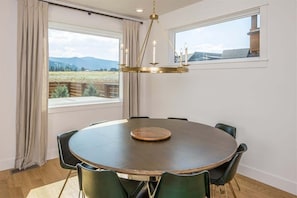 A dining area with a round table, six chairs, a chandelier, and large windows offering a view of the outdoors. - Opulent 4 Bedroom Townhouse (Big Sky)