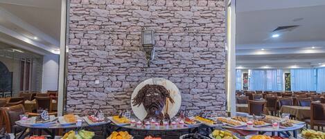 Un buffet con diversi cibi e un muro in pietra con una testa decorativa sullo sfondo.