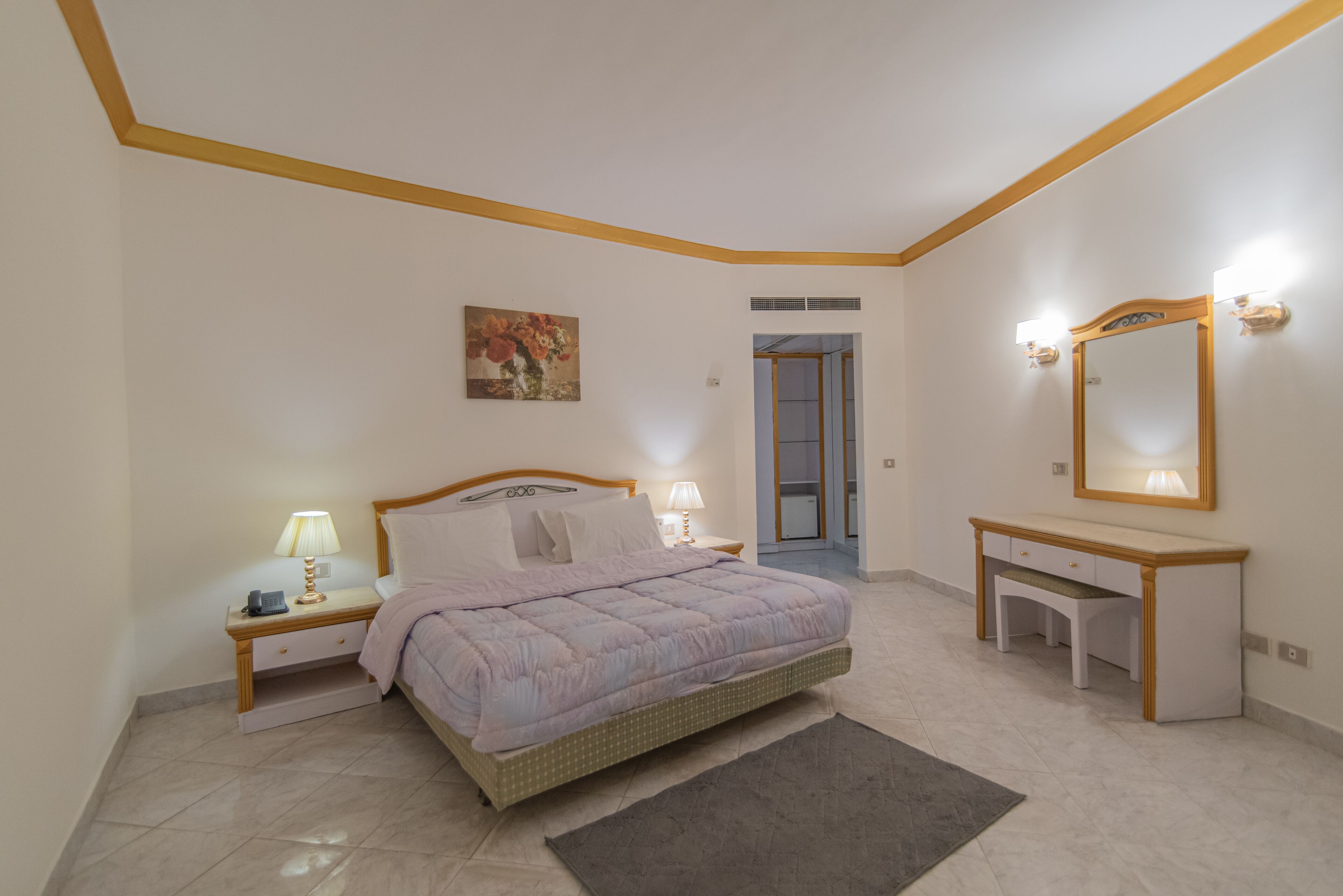 Un dormitorio con cama, mesitas de noche, un escritorio, un espejo y un cuadro en la pared.