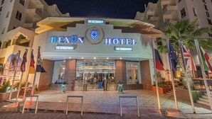 El exterior del Hotel Dexion, con una entrada destacada, banderas y una fachada bien iluminada.