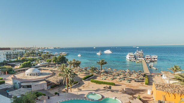 Un complejo turístico en la costa con piscina, sombrillas de playa y barcos en el agua.