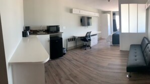 A modern kitchen with a microwave, refrigerator, and a small island. There is a black office chair and a black sofa in a living area with a large window. - Crystal Inn (Port Arthur)