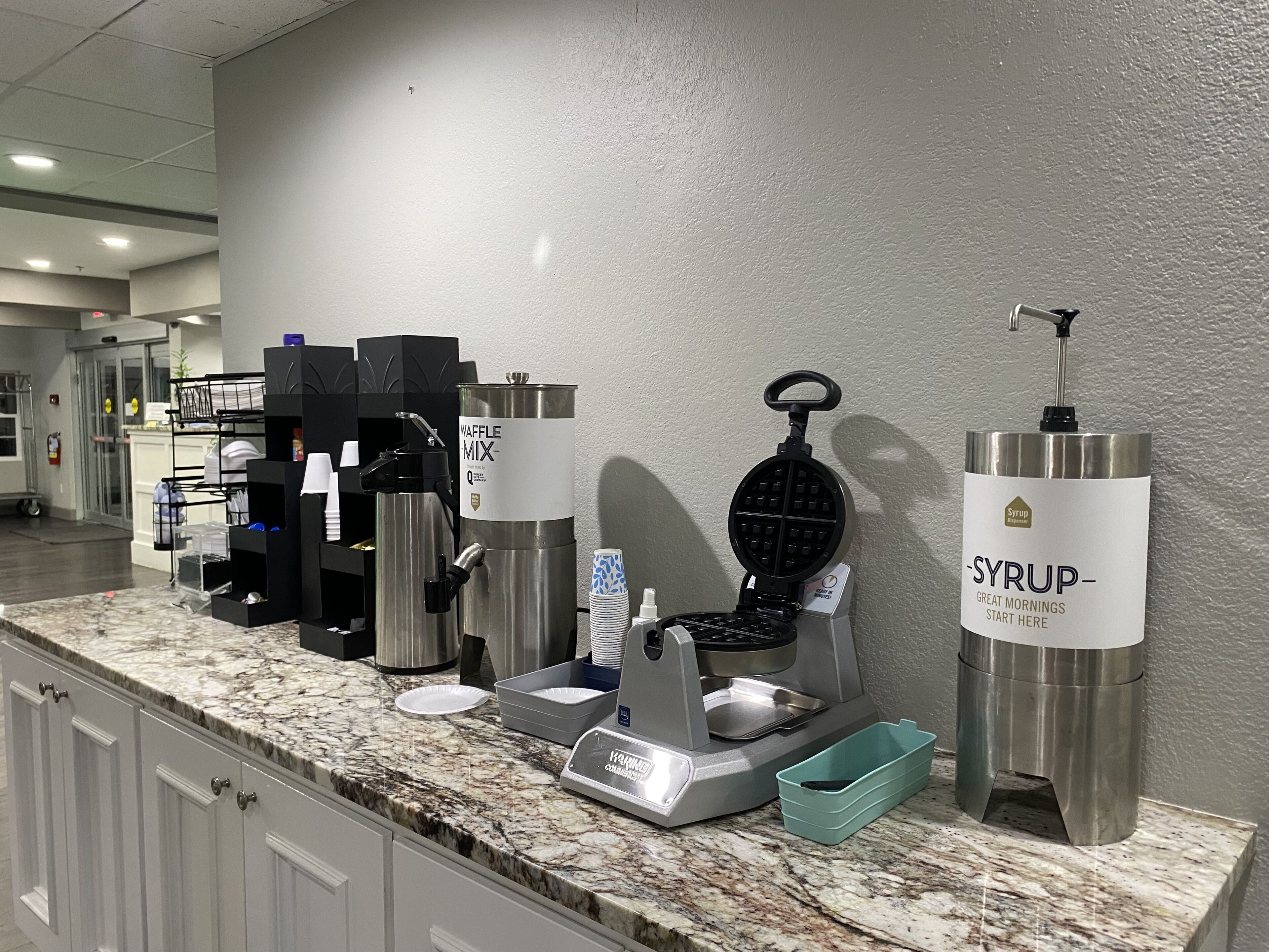 Estação de pequeno-almoço de serviço balcão com máquina de waffles, cafeteira e dispensador de xarope.