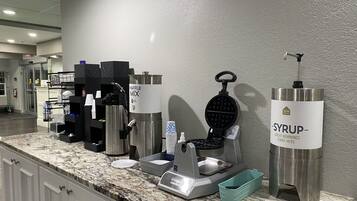 Estação de pequeno-almoço de serviço balcão com máquina de waffles, cafeteira e dispensador de xarope.
