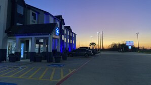 A hotel entrance with a sign for Crystal Inn, a parking lot with handicapped parking, and a sunset in the background. - Crystal Inn (Port Arthur)