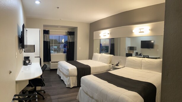 A hotel room with two single beds, a desk with a chair, a TV, a microwave, and a large mirror. - Crystal Inn (Port Arthur)