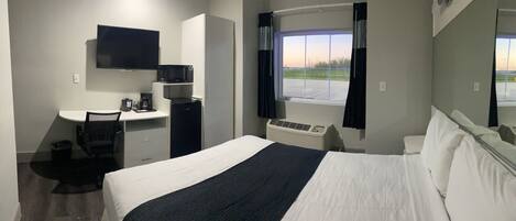 Een hotelkamer met een bed, een bureau met stoel, een televisie, een raam met gordijnen en een airconditioning.