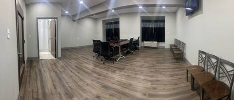 A conference room with a long table and chairs, wooden flooring, and a ceiling with recessed lighting.
