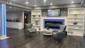 A modern living room with two armchairs, a coffee table, and a fireplace. There is a television mounted above the fireplace and a kitchen area in the background. - Crystal Inn (Port Arthur)
