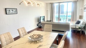Un saló modern amb zona de menjador, que destaca per una taula de marbre, cadires de cuir blanc, un sofà i una finestra gran amb vista a la ciutat.