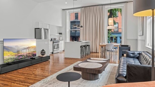 Ein modernes Wohnzimmer mit Flachbildfernseher, Ledersofa und einem Essbereich mit Tisch und Stühlen.