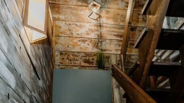 Un escalier en bois, doté d’une rampe, mène à un palier où est fixée une lampe.