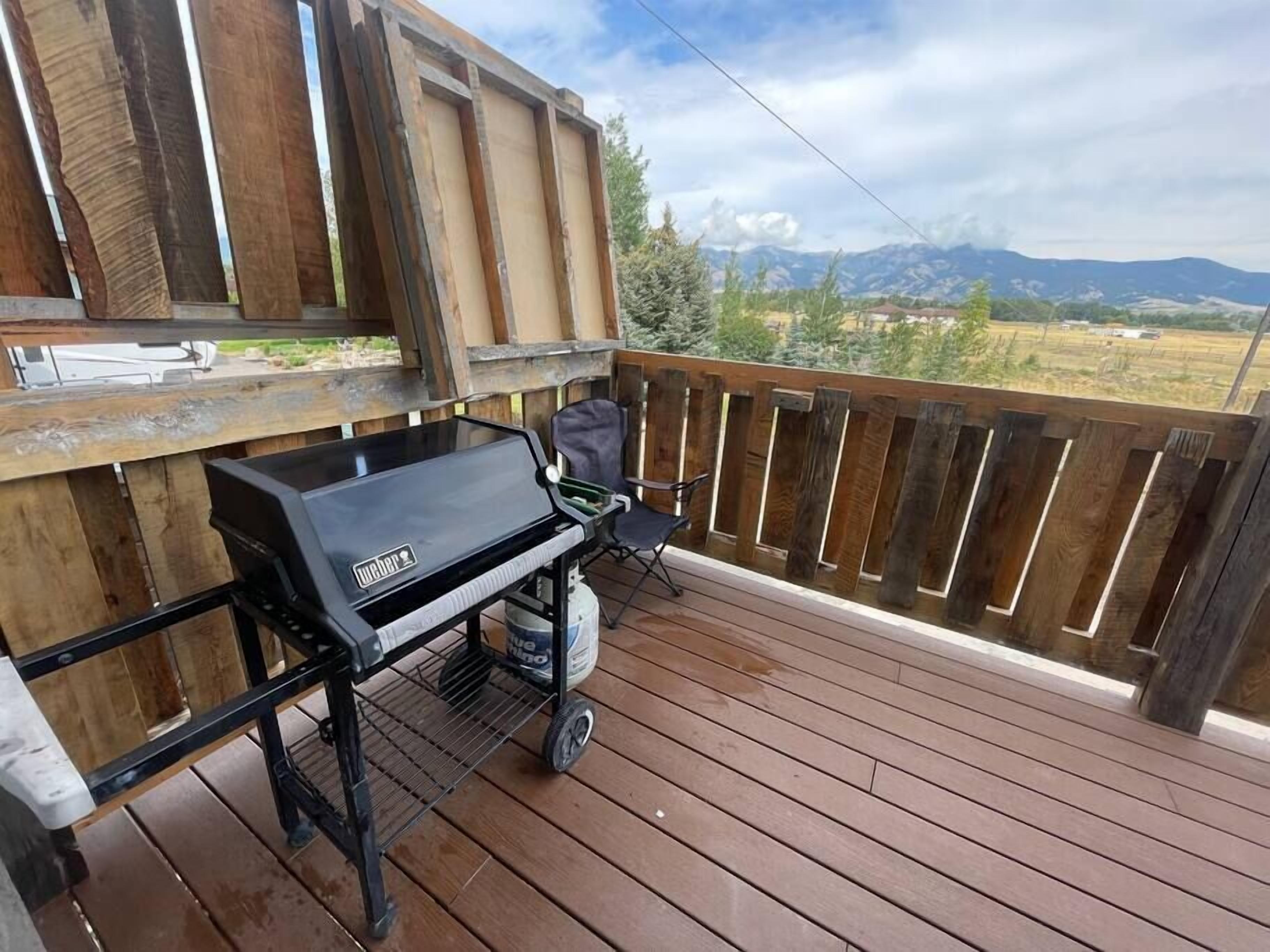 A wooden deck with a grill and a chair, overlooking a mountainous landscape.
