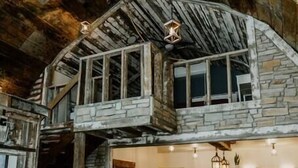 Un intérieur rustique comprenant une chambre à coucher située en mezzanine, un coin repas et un salon avec des canapés en cuir.