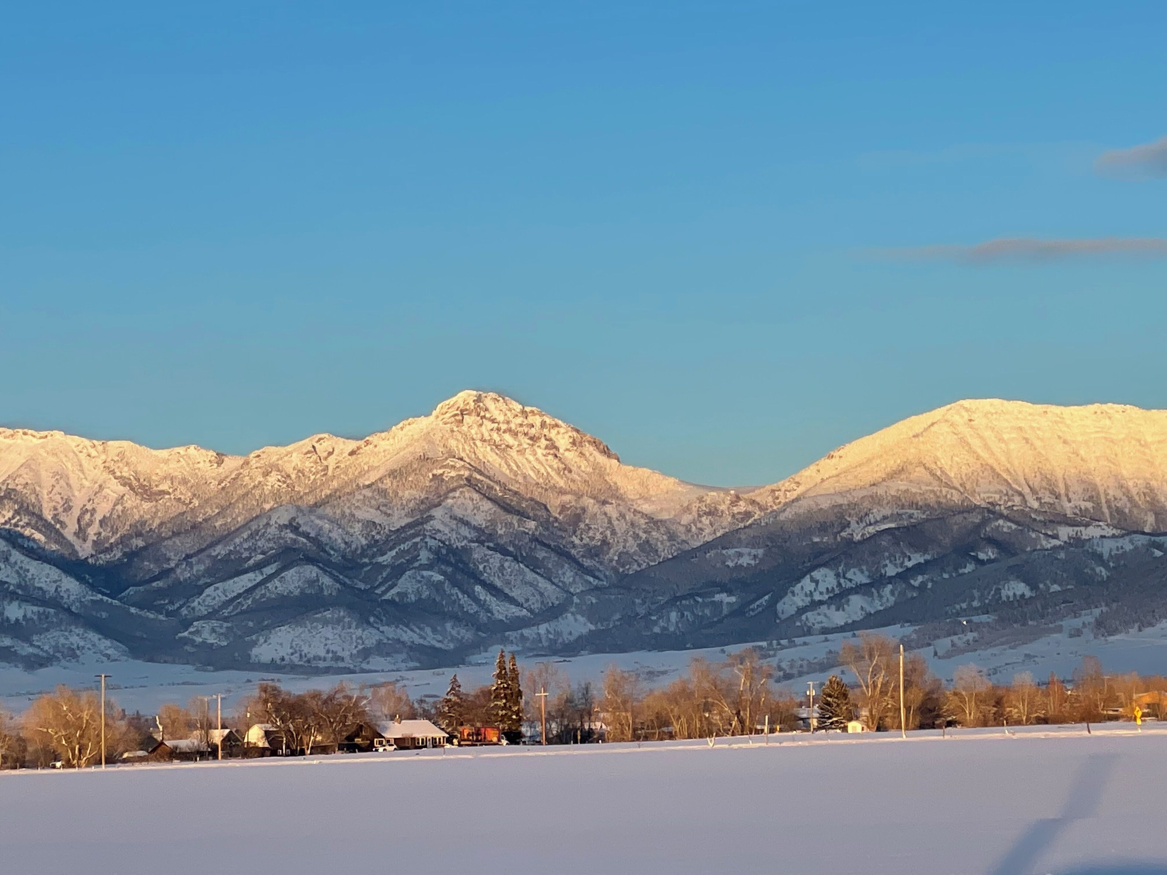 A snow-covered landscape with mountains in the background and a few buildings in the foreground.