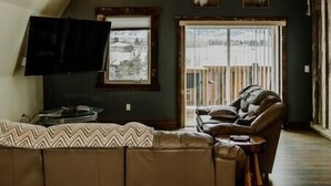 Un salon chaleureux avec un canapé d’angle, un fauteuil en cuir et un téléviseur à écran plat fixé au mur.