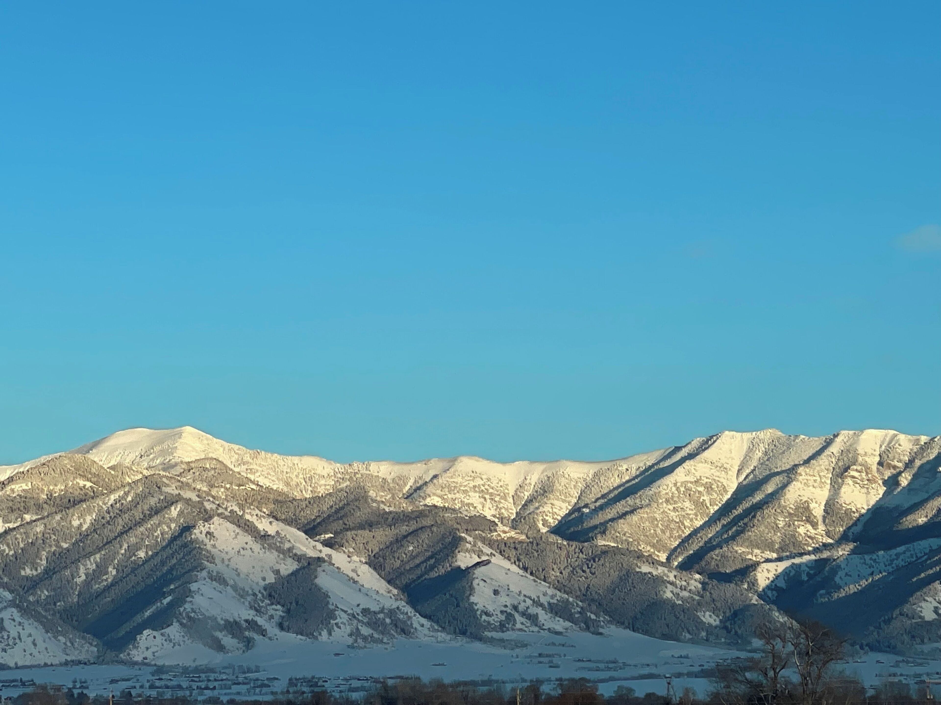 Une chaîne de montagnes aux sommets enneigés, sous un ciel bleu et dégagé.
