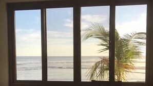 Een kamer met een houten tafel, een fruitschaal en uitzicht op de oceaan door grote ramen.