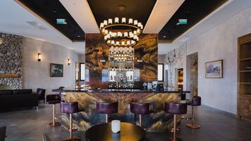 A bar area with a marble countertop, multiple bar stools, and a central chandelier.