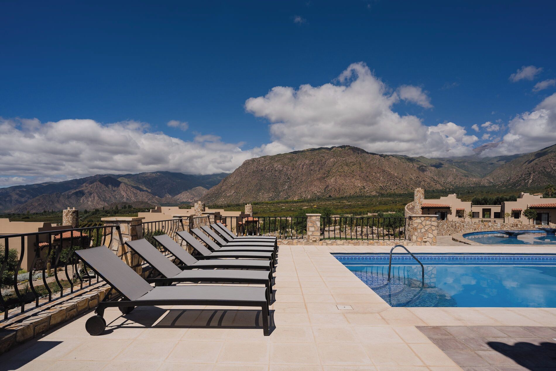 A rooftop pool area with lounge chairs and a swimming pool, surrounded by mountains and clear skies.