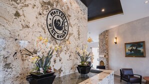 Een receptie met een marmeren muur, een logo, twee bloemstukken, een stenen muur, een schilderij en een lederen fauteuil.