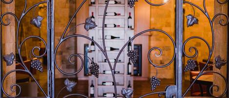 Una elaborada puerta de hierro forjado con diseños de vid, que da acceso a una bodega con botellas de vino ordenadas.