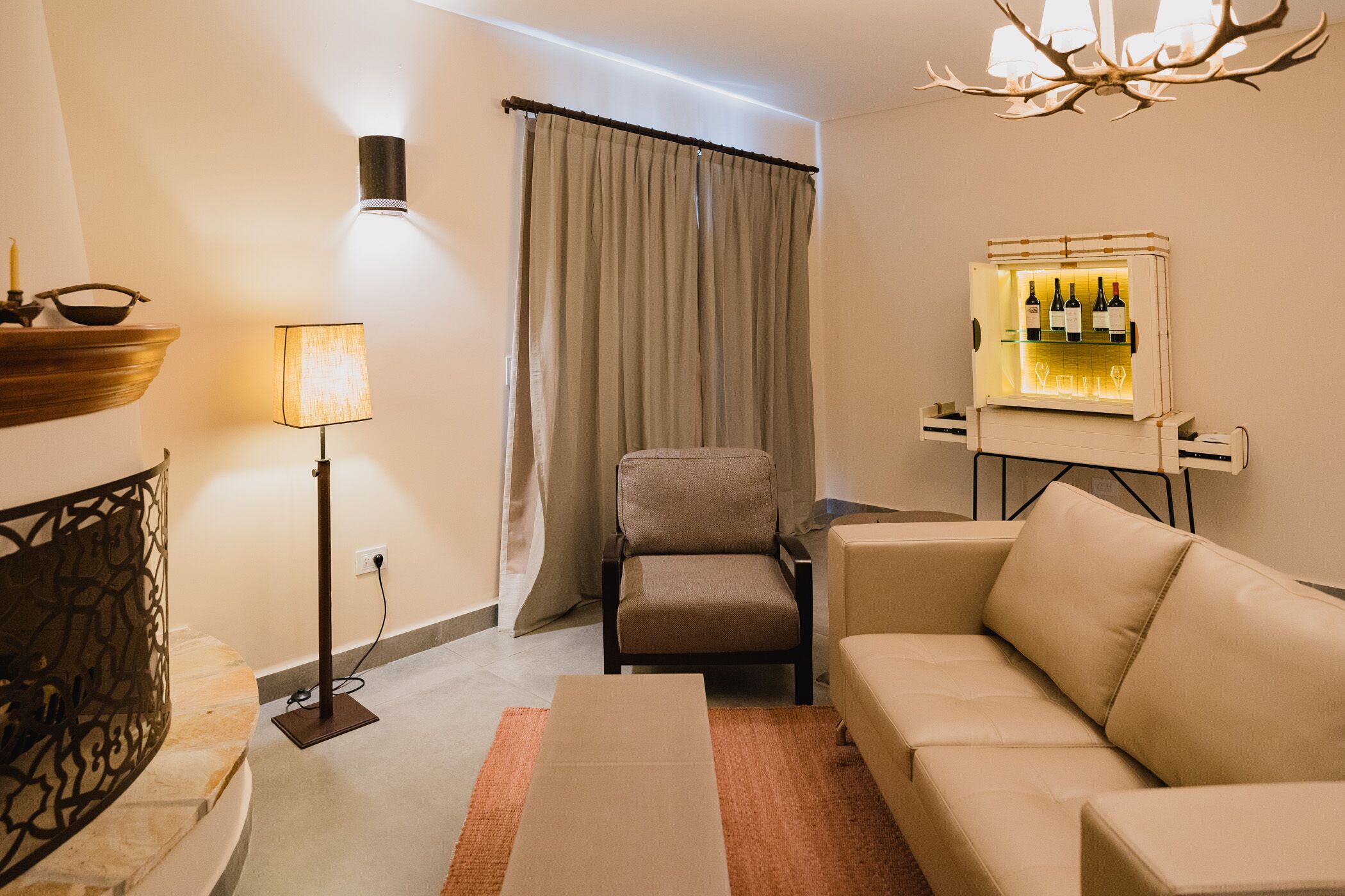 A modern living room with a beige sofa, a floor lamp, a chair, a small table, and a wine refrigerator.
