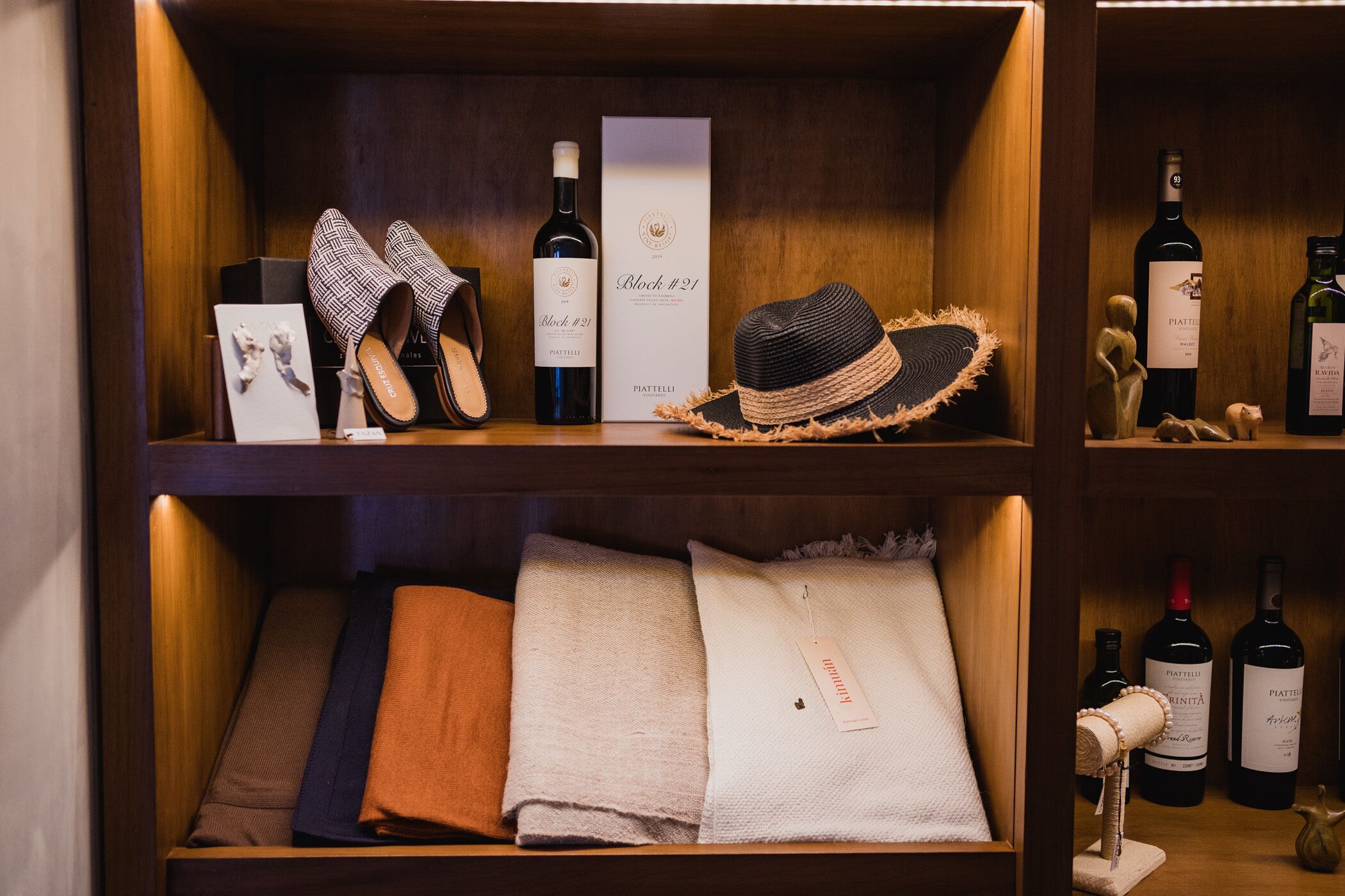 A wooden shelf with a pair of patterned slippers, a bottle of wine, a hat, and a box labeled "Block #21".