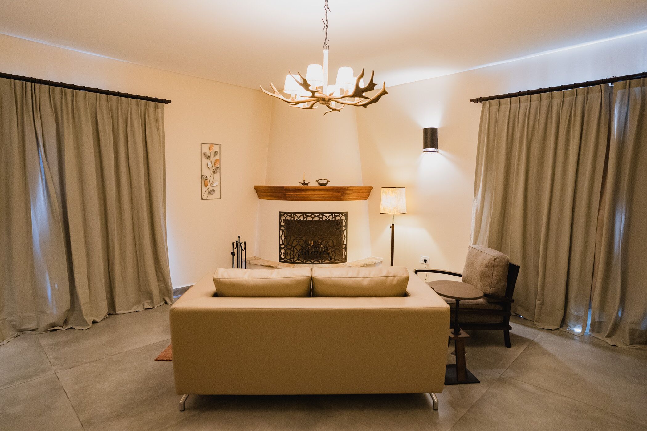 A modern living room with a large sofa, a fireplace, a chandelier, and curtains.