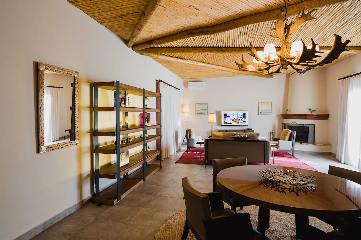 Ein großzügiger Wohnbereich mit hoher Decke, Holzboden, einem Esstisch mit Stühlen, einem Fernseher und einem Kamin.