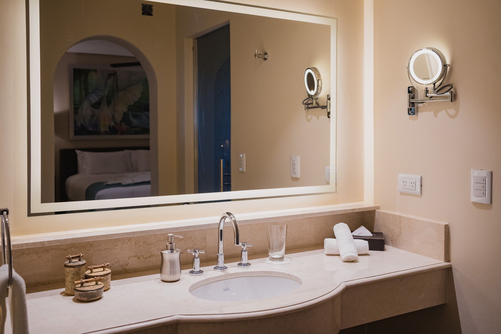 A bathroom with a large mirror, a sink, and a towel rack.
