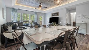 A spacious living room with a large dining table, comfortable seating, and a ceiling fan.