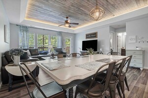 A modern living room with a dining area, a ceiling fan, and a flat-screen TV.