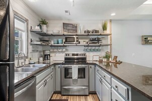 A modern kitchen with stainless steel appliances, wooden shelves, and a coffee station.