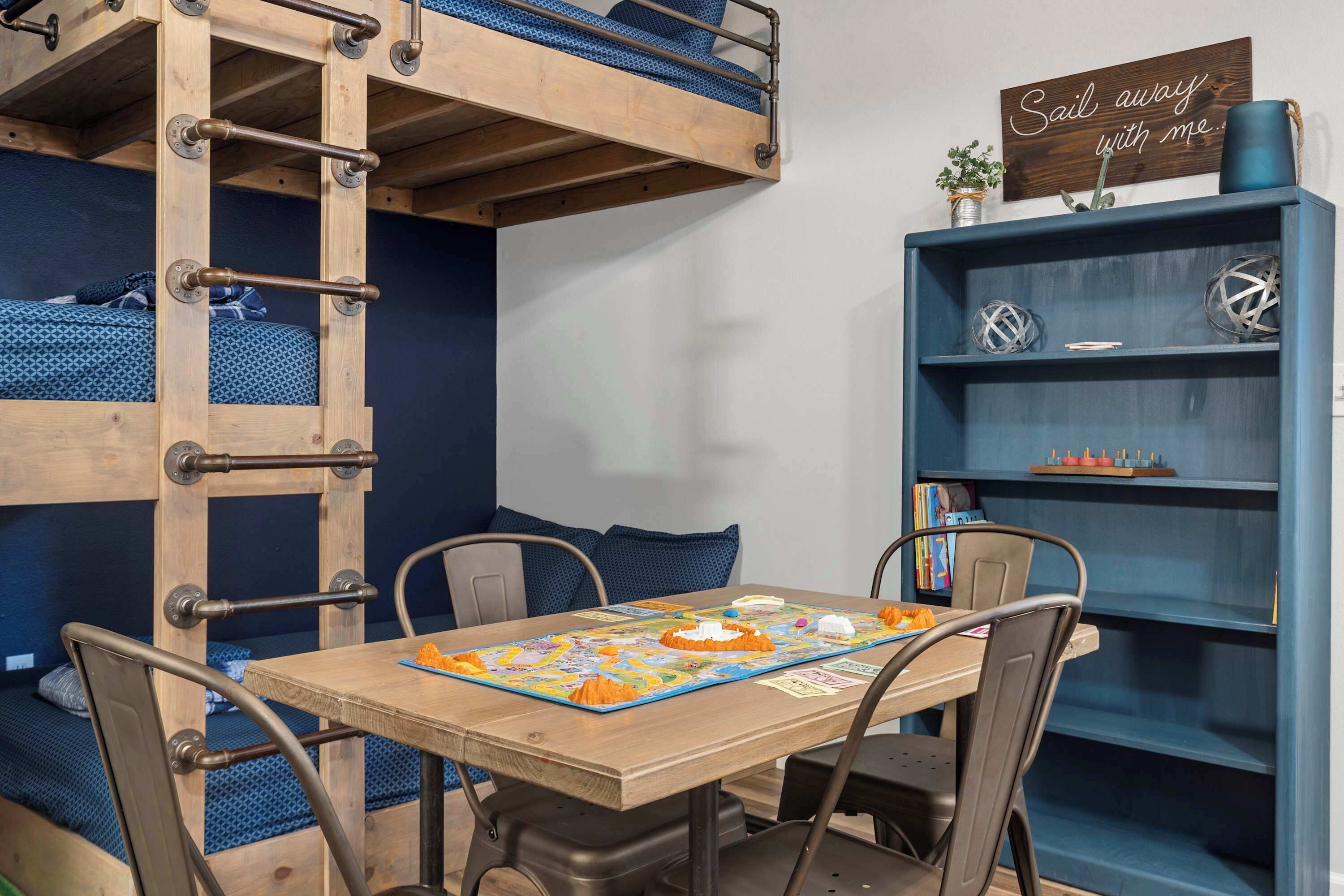 A bunk bed with a ladder, a table with a board game, and a bookshelf with decorative items.