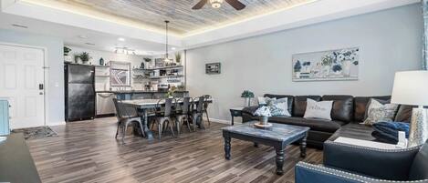A modern living room with a dining area, a ceiling fan, and a kitchen in the background.