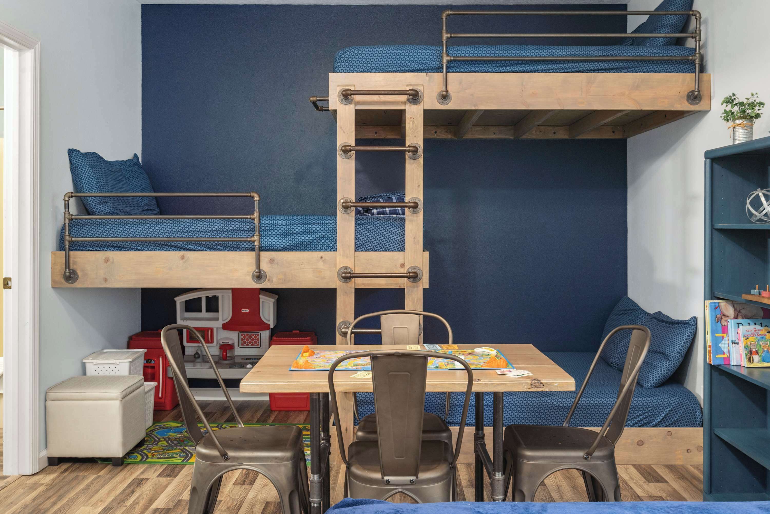 Habitación con literas, una mesa, sillas y una estantería.