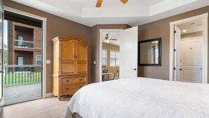 Une chambre dotée d’un grand lit, d’une armoire en bois, d’un ventilateur de plafond et d’une porte-fenêtre coulissante donnant sur un balcon.