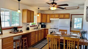 Una cocina con armarios de madera, una mesa de comedor, sillas, un ventilador de techo y un refrigerador.