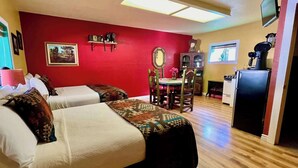 Una habitación con dos camas, una mesa de comedor, sillas, un televisor y un refrigerador.
